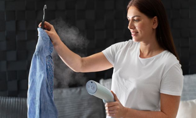 a woman wearing a white t shirt is holding a shirt from her one hand and a steam iron from her second hand