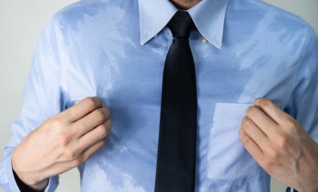a man wearing dark blue shirt with black tie, the shirt is full of sweat.