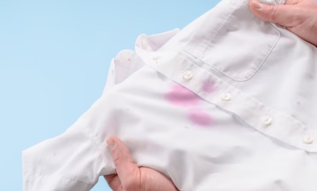 a person is holding a white color shirt that has some light pink stains on it