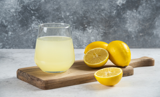 a cup of lemon juice along with whole lemons placed over a chopping board