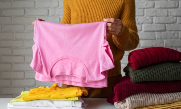 a girls is wearing a yellow sweater and she is holding a pink t shirt